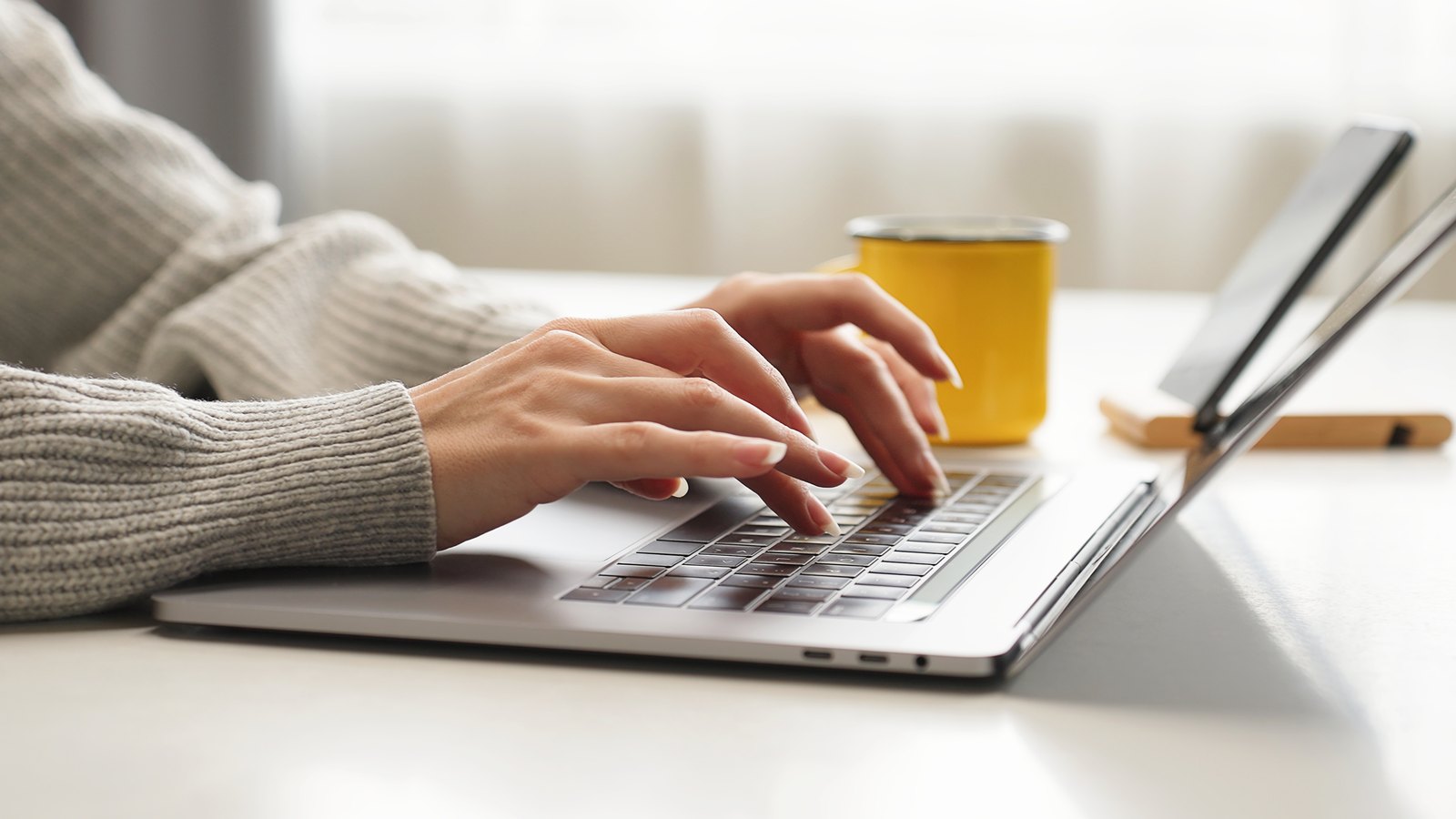 Hands typing on a laptop at a bright desk