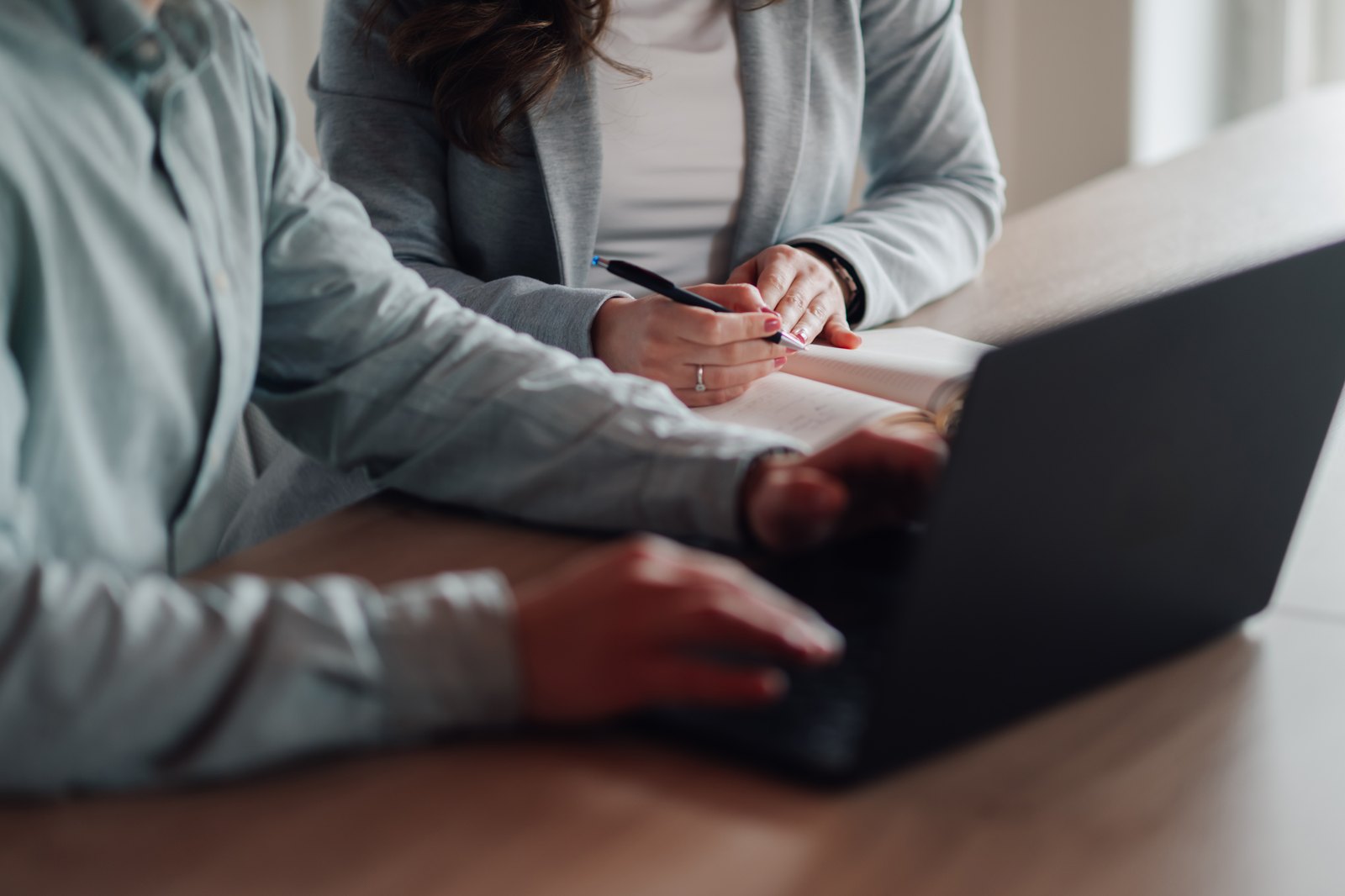 Two colleagues working together at a laptop, one taking notes